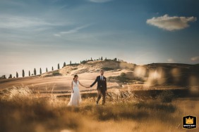 In the rolling landscape of Crete Senesi, Tuscany, the newlyweds stroll during a stunning couple portrait, capturing the romantic and unique beauty of the Italian countryside.